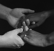 black and white image of couple holding hands showing round solitaire engagement ring in foreground